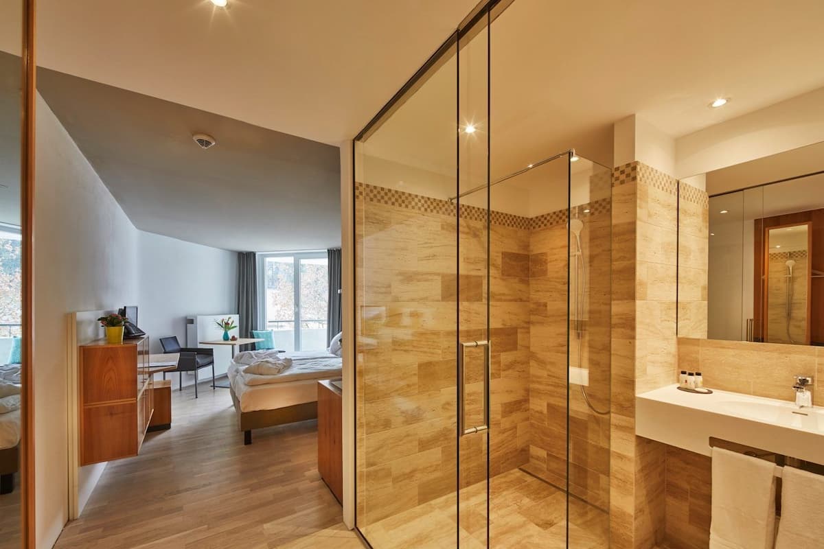 Une chambre d’hôtel moderne dotée d’une douche en verre, d’un grand miroir et d’un plancher en bois.