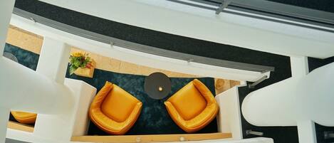 A boat interior with two yellow cushioned chairs, a small table with a plant, and a dark blue carpet.