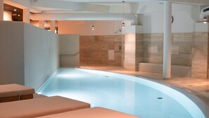 A modern indoor pool with a curved edge, seating areas, and a shower area with patterned tiles.