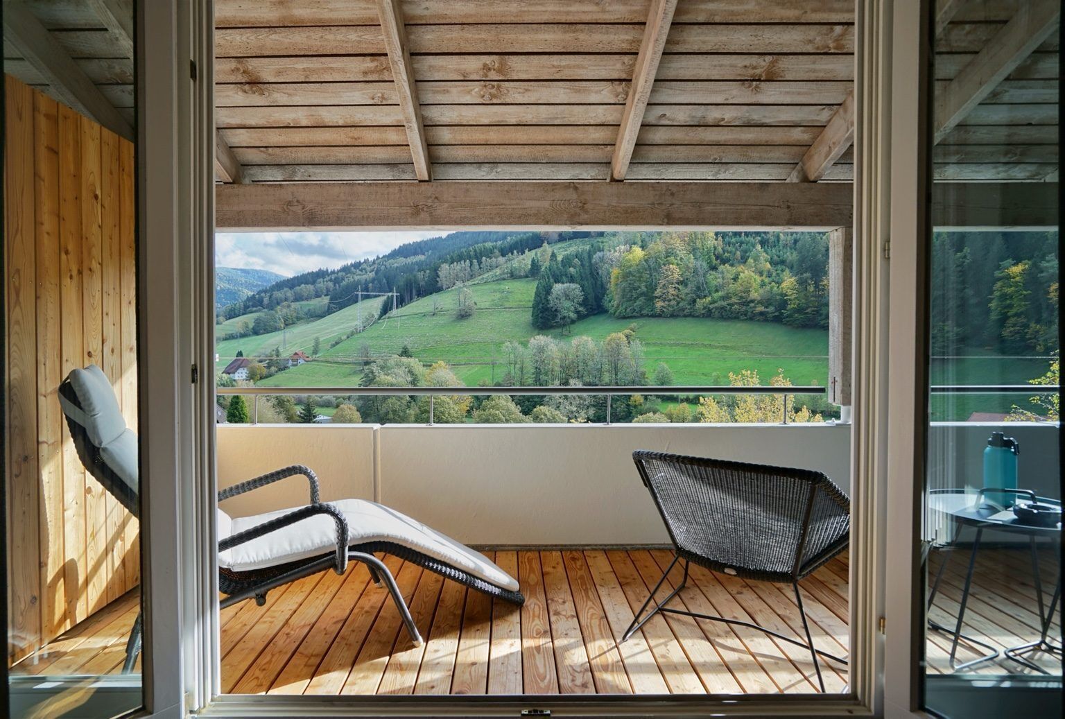 Un balcon doté d’un plancher en bois, de deux chaises et offrant une vue sur un paysage verdoyant.