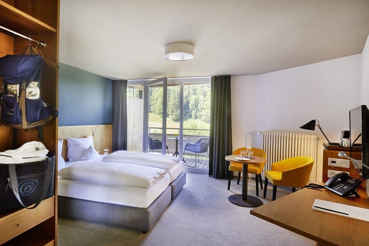 Une chambre d’hôtel avec un lit, un bureau équipé d’un ordinateur, une chaise et une vue sur l’extérieur.