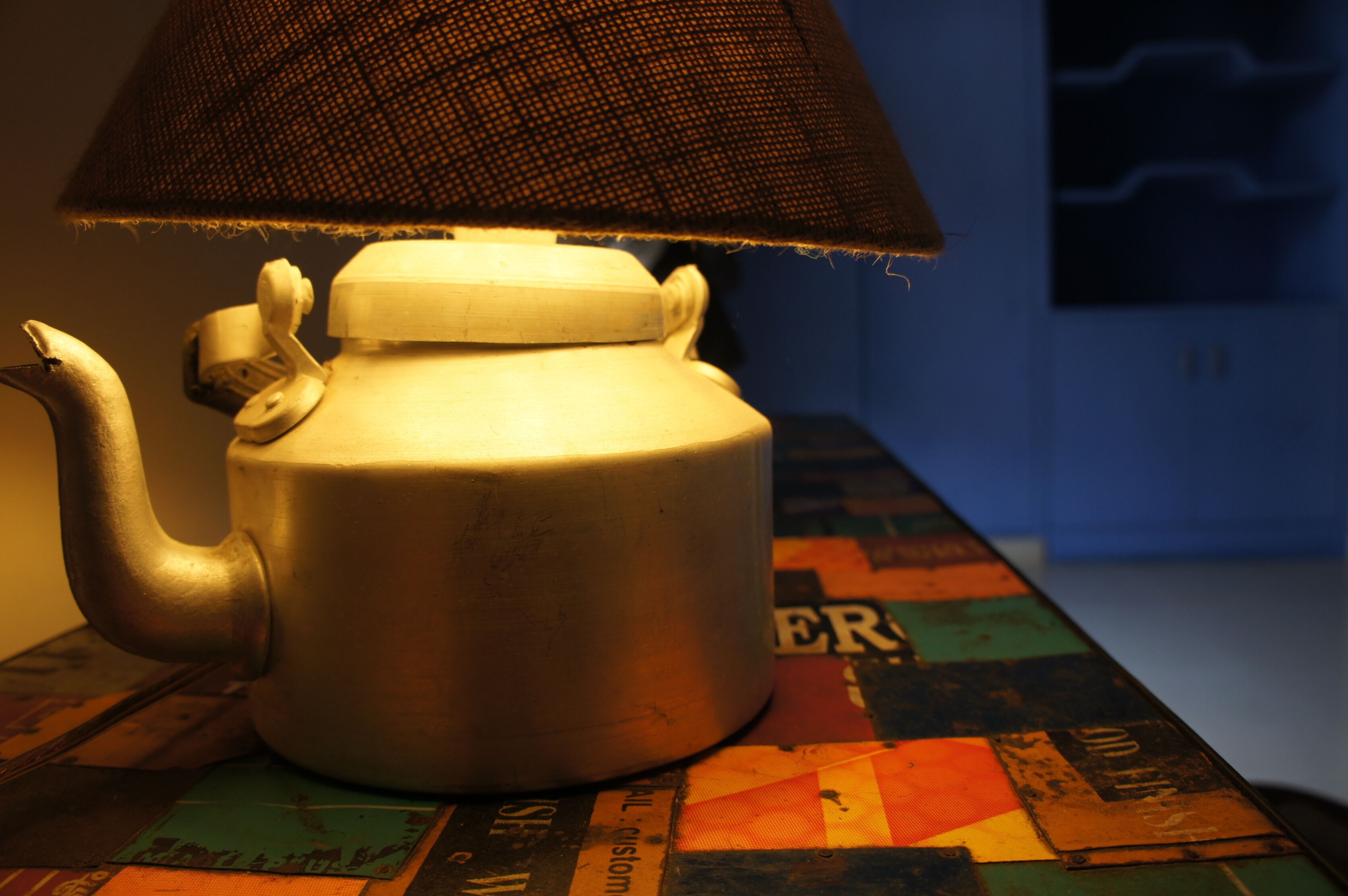 A ceramic teapot with a textured lid and a handle, placed on a table with a colorful geometric-patterned tablecloth.