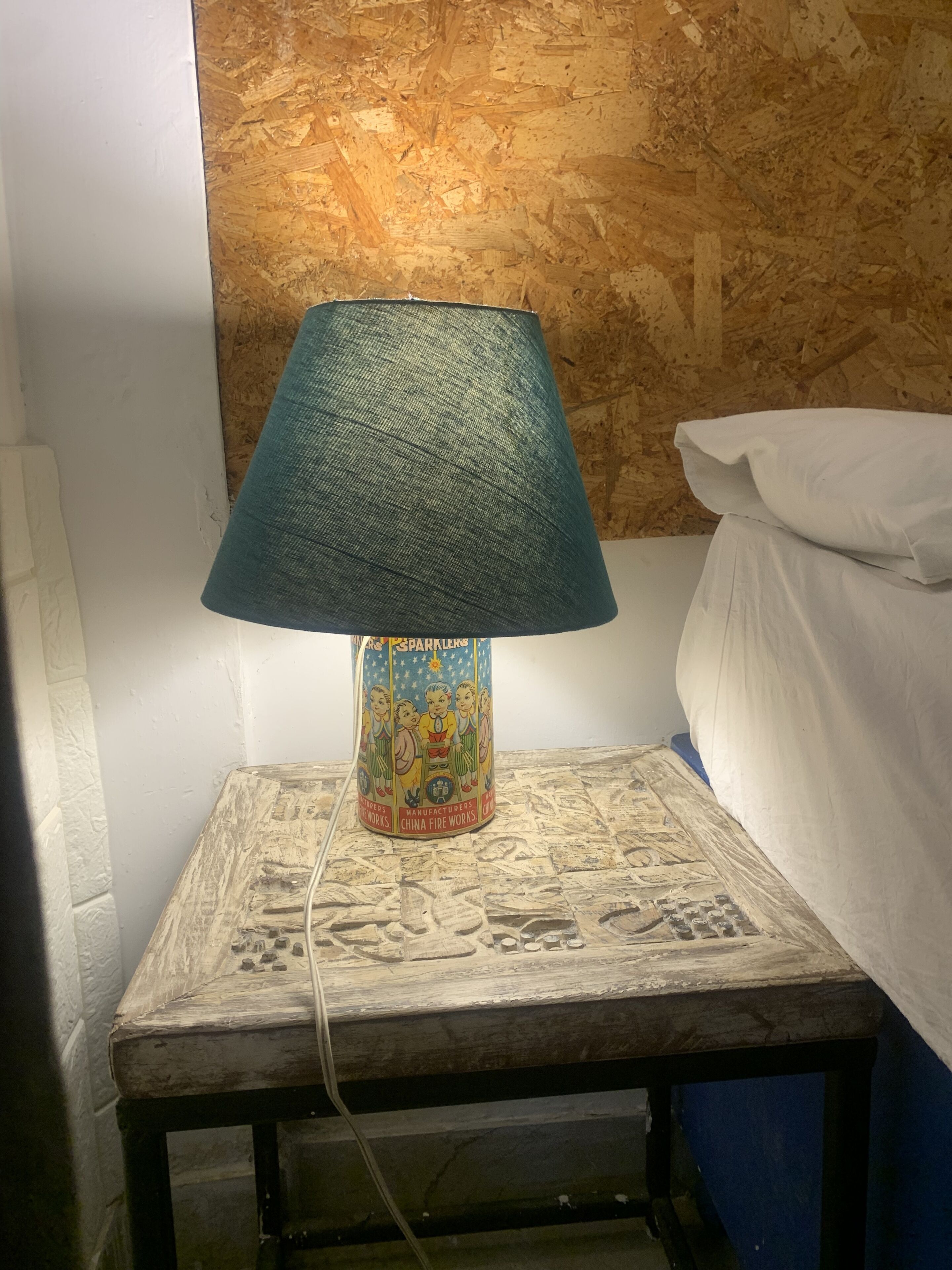 A bedside table with a lamp, a bed, and a wall with a textured pattern.