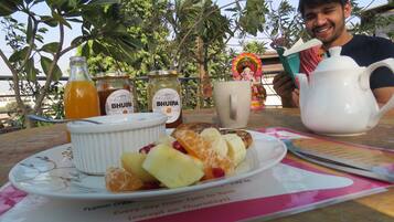 Une table mise pour le petit-déjeuner, avec une assiette de fruits, deux bouteilles de jus, une théière et une tasse, ainsi qu’un menu.