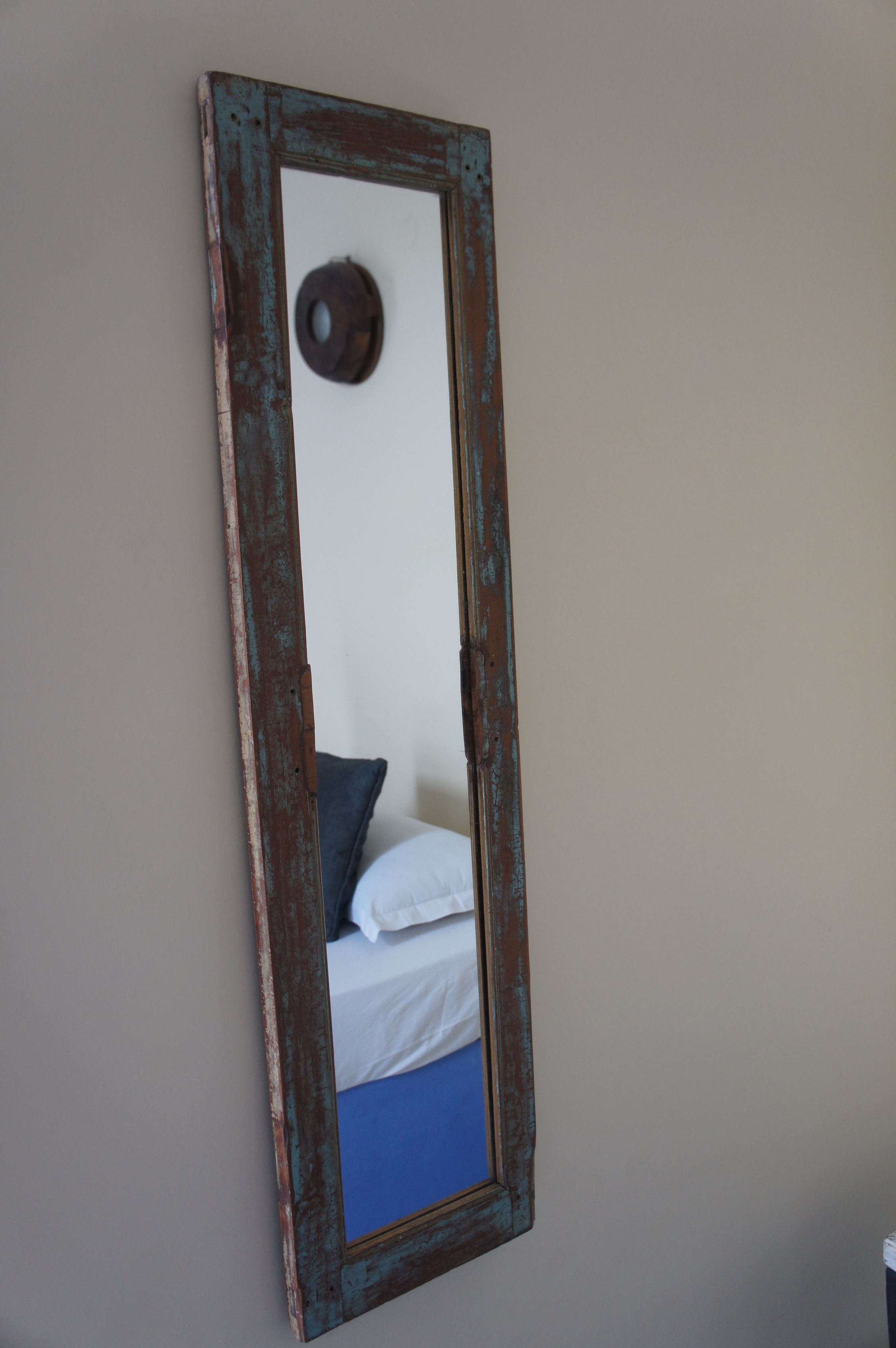 A mirror with a rustic frame reflecting a bed with white bedding and a blue pillow.