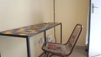 Une petite pièce avec une table recouverte d’une nappe colorée, une chaise avec un journal, une prise électrique et une porte dotée d’une poignée.