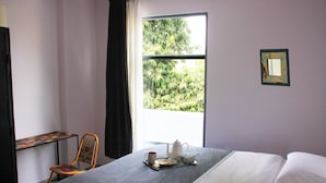 A neatly made bed with a tray of tea set, a chair, and a window with a view of greenery. - Bed & Chai Guest House (New Delhi)