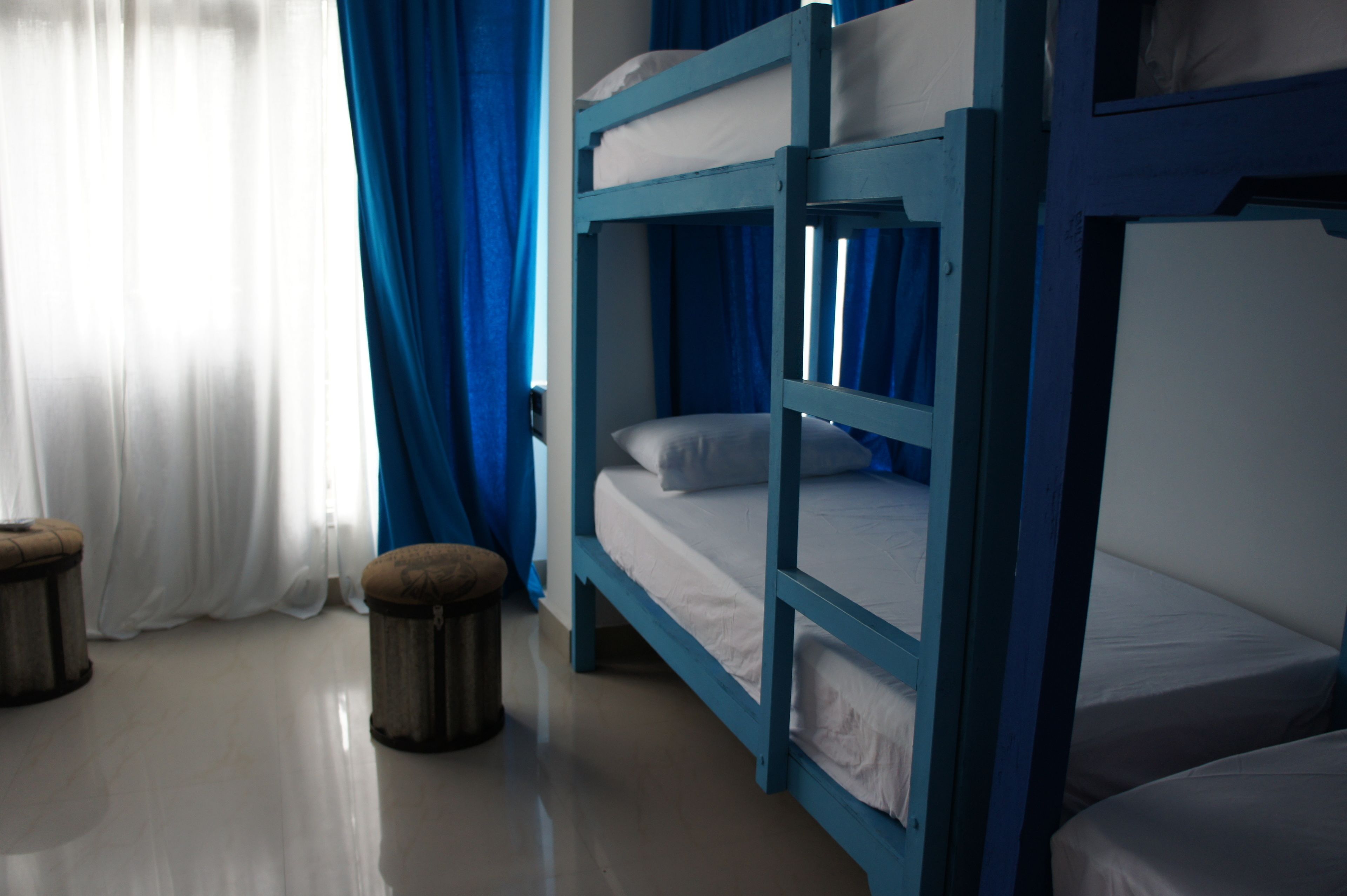 A bunk bed room with a window, curtains, and a trash bin.