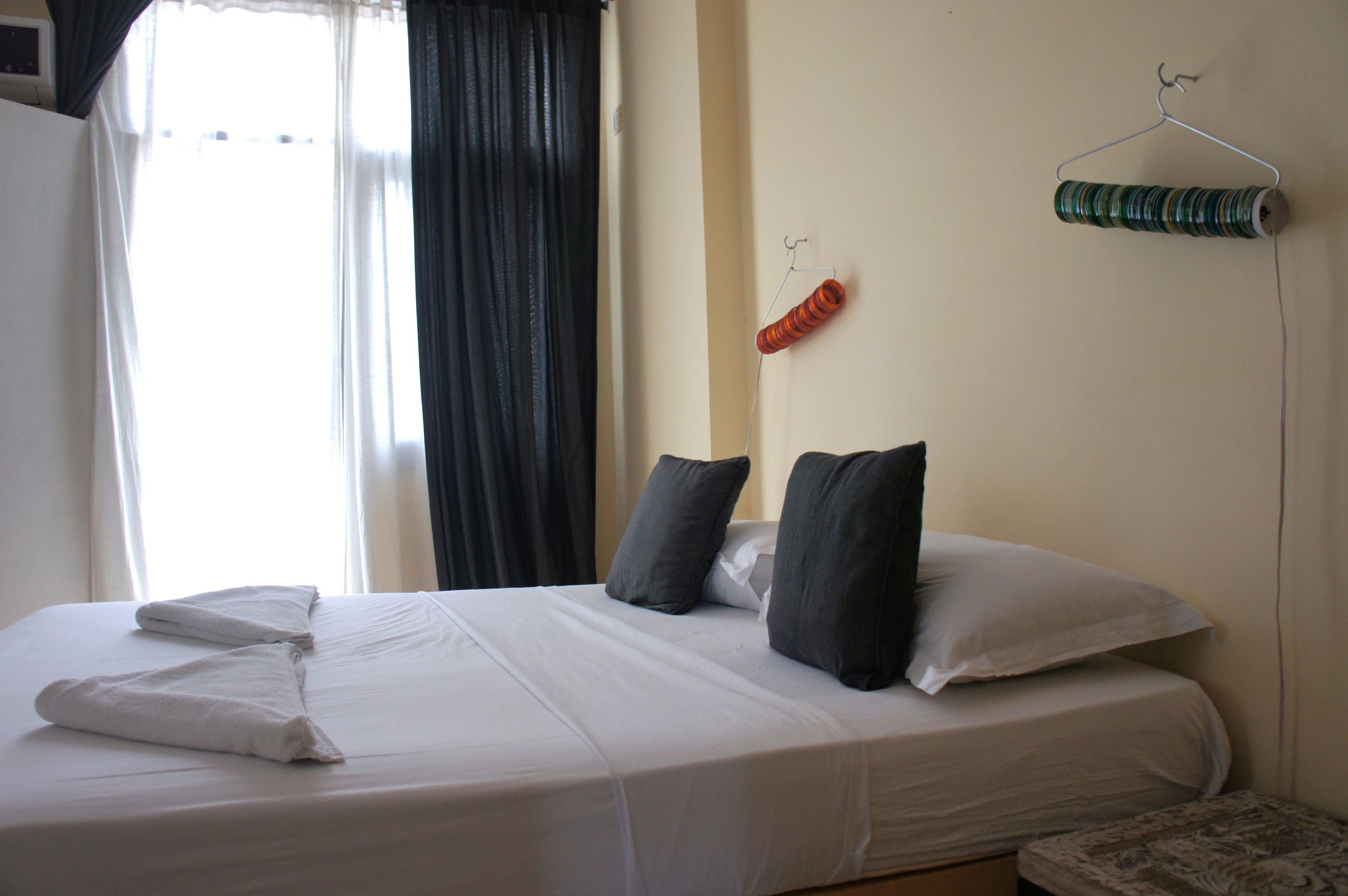 A neatly made bed with pillows, a hanging spool of thread, and a window with curtains.