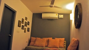 A bedroom with a bed, patterned pillows, a ceiling fan, and an air conditioning unit. - Bed & Chai Guest House (New Delhi)
