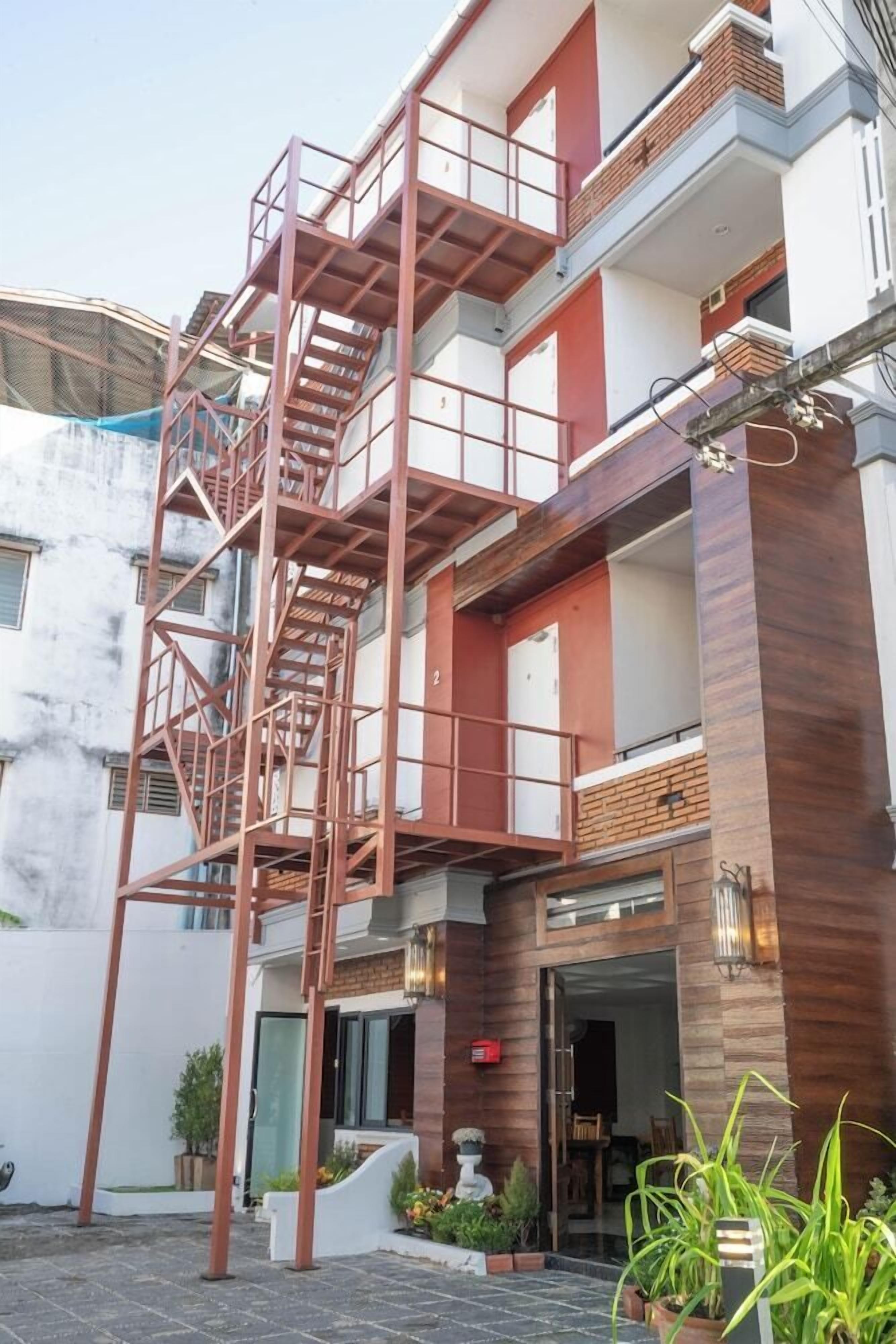 A multi-story building with a prominent external staircase, a gated entrance, and a small outdoor seating area.