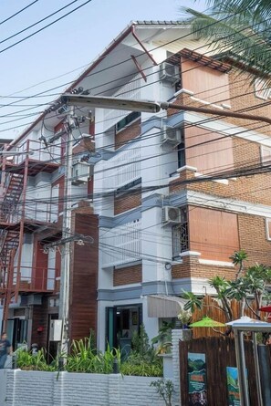 Un edificio de varios pisos con un diseño arquitectónico moderno, que combina paredes exteriores de ladrillo y blanco, y una escalera visible en el lado izquierdo.