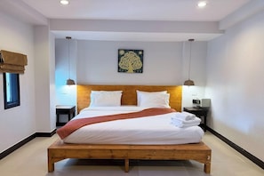 Une chambre à coucher avec un lit en bois, une literie blanche, une table de chevet avec une lampe, une œuvre d’art accrochée au mur et une fenêtre avec des stores.