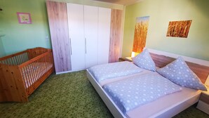 A bedroom with a bed, a crib, a wardrobe, and a wall with a picture.