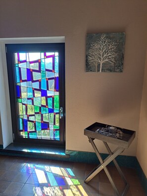 A door with a stained glass design, a wall-mounted artwork of a tree, and a small table with decorative items.