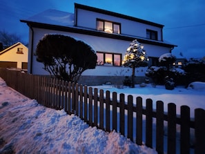 A two-story house with a snow-covered yard and a wooden fence.