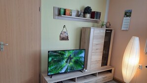A room with a television on a wooden stand, a cabinet, a shelf with books and decorative items, and a wall calendar.