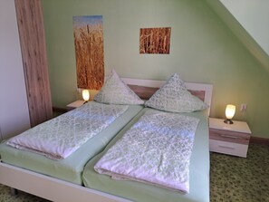 A double bed with two pillows, a bedside table with a lamp, and a wall with two paintings.
