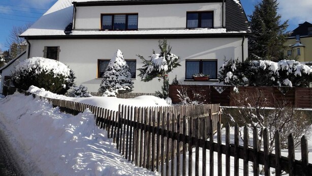 A two-story house with a snow-covered roof and a wooden fence in front.