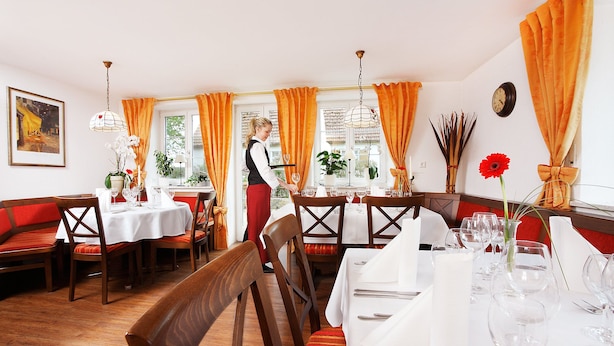 Een restaurant met houten meubels, witte tafelkleden en oranje gordijnen.