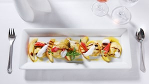 Een wit, rechthoekig bord met een dessert van fruit en slagroom, samen met twee wijnglazen en een servet.