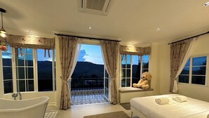 A bedroom with a large bed, a bathtub, and a view of mountains through the window. - Misty English Cottage (Khao Kho)