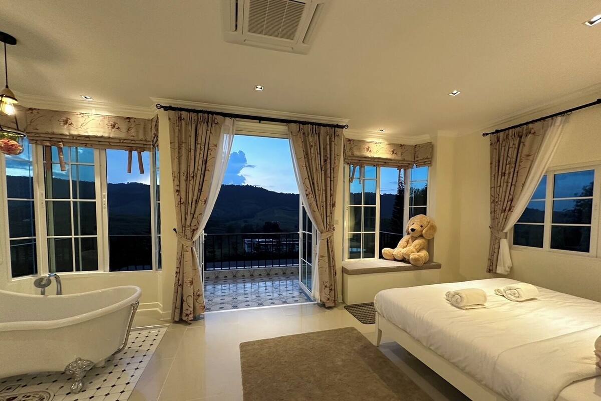 A bedroom with a large bed, a bathtub, and a view of mountains through the window.