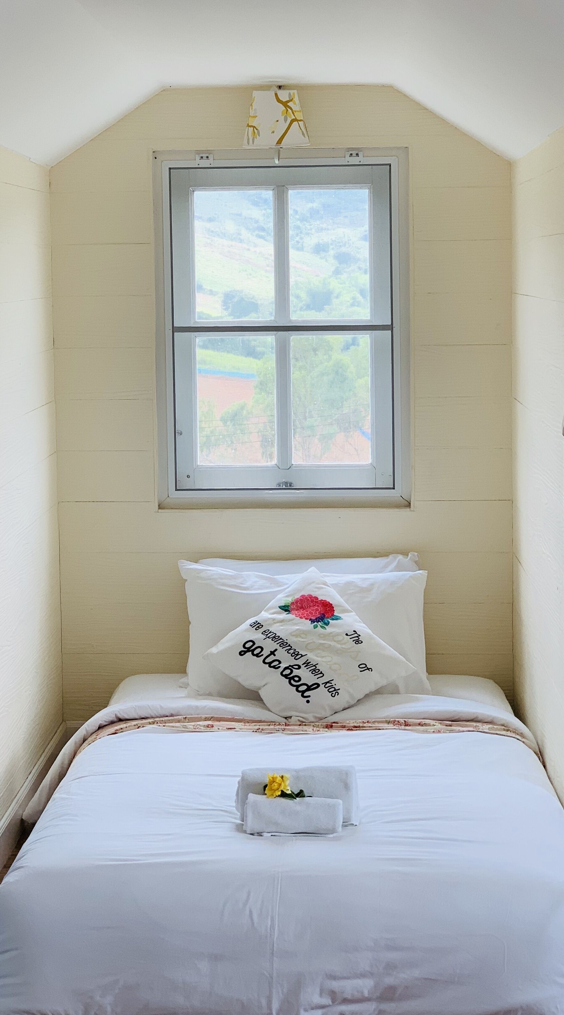 Une chambre à coucher avec un lit, des oreillers, une fenêtre et une vue sur la verdure.