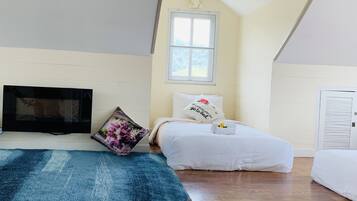 Un dormitorio con techo inclinado, una ventana, una cama con ropa de cama blanca, una alfombra azul y un televisor montado en la pared.