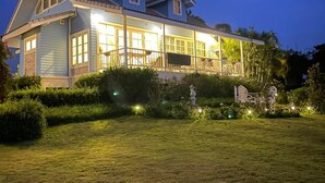 A large, two-story house with a covered porch and a well-lit garden at dusk. - Misty English Cottage (Khao Kho)