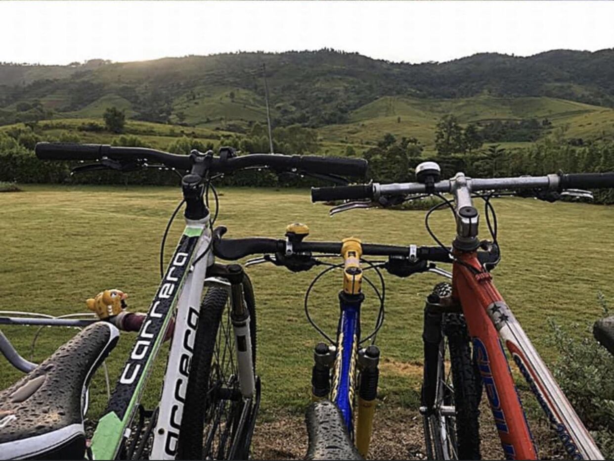 Two bicycles parked in a grassy field with a hilly landscape in the background.