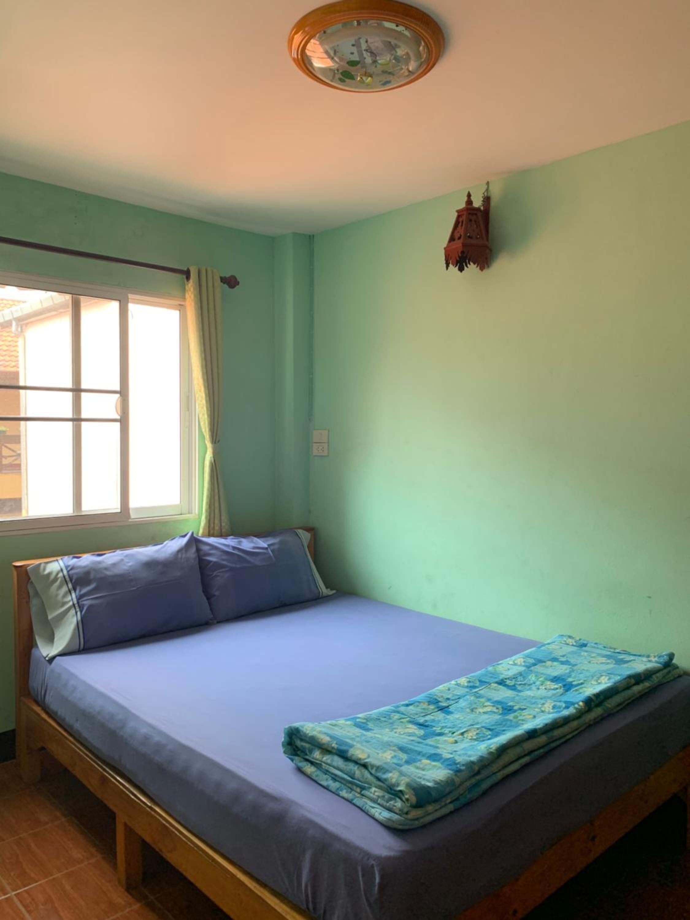 A room with a bed, a window with curtains, a ceiling fan, and a wall-mounted light fixture.