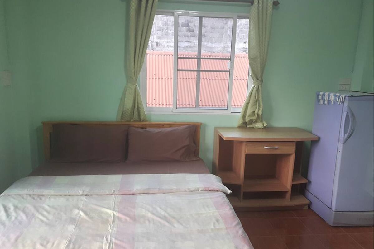 A bedroom with a bed, a desk, and a refrigerator.