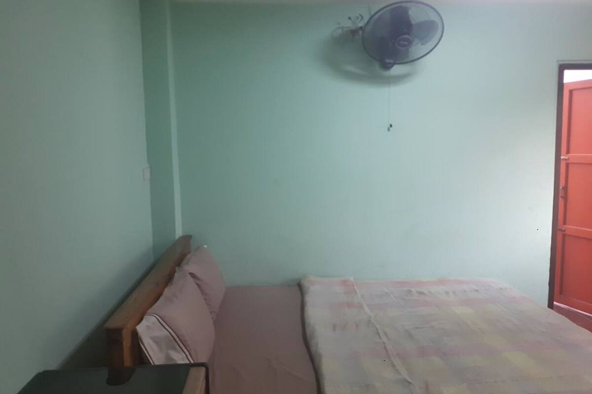 A room with a bed, a wooden headboard, a wall-mounted fan, and a door.