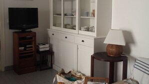 A living room with a television on a wooden stand, a white cabinet with glass doors, and a small table with a lamp. - Cozy 2-Bedroom House near Arcachon Center & Beach (Arcachon)