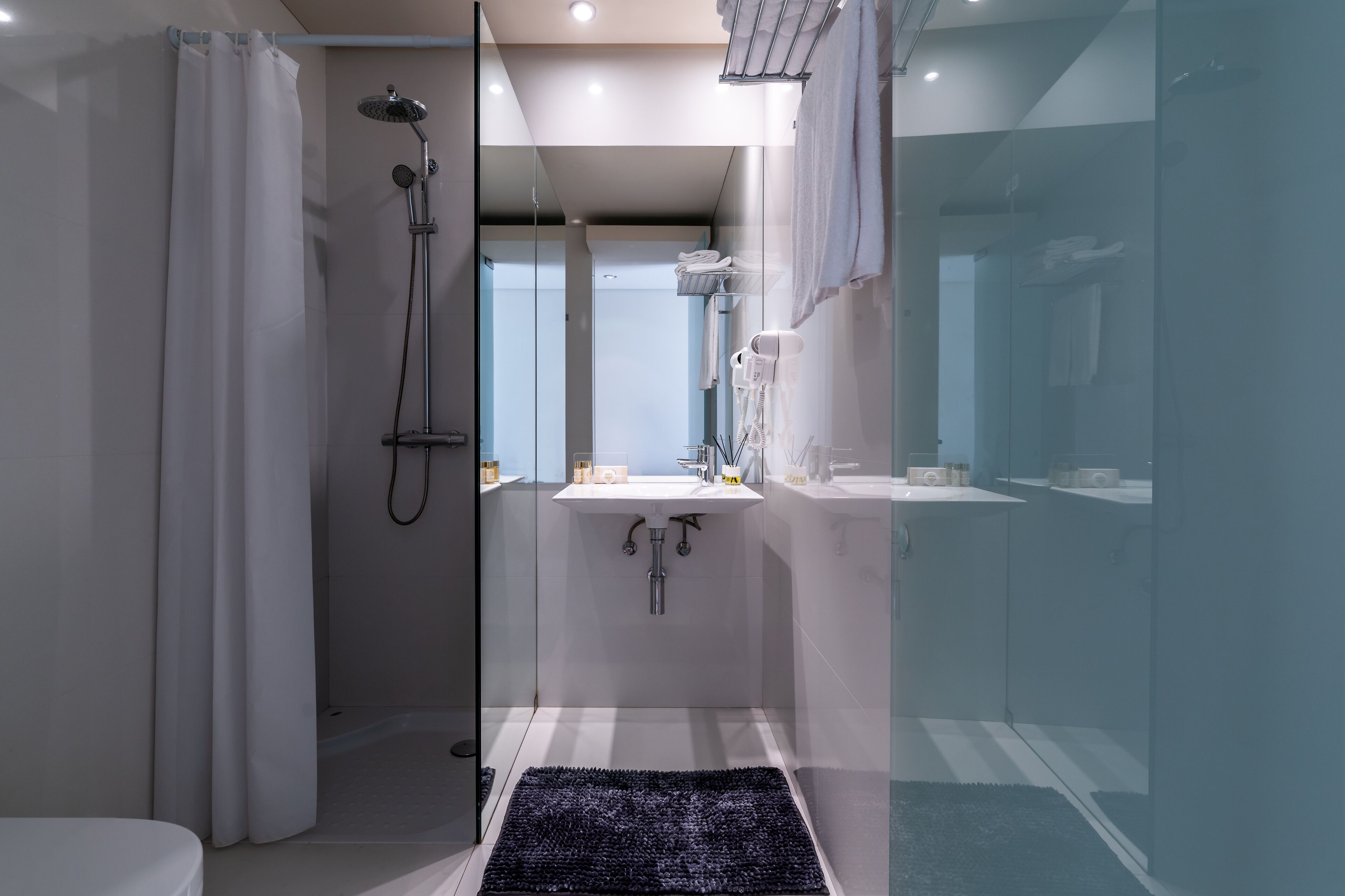A modern bathroom with a glass shower enclosure, a white sink, and a black rug.