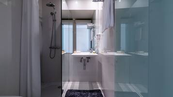 A modern bathroom with a glass shower enclosure, a white sink, and a black rug.
