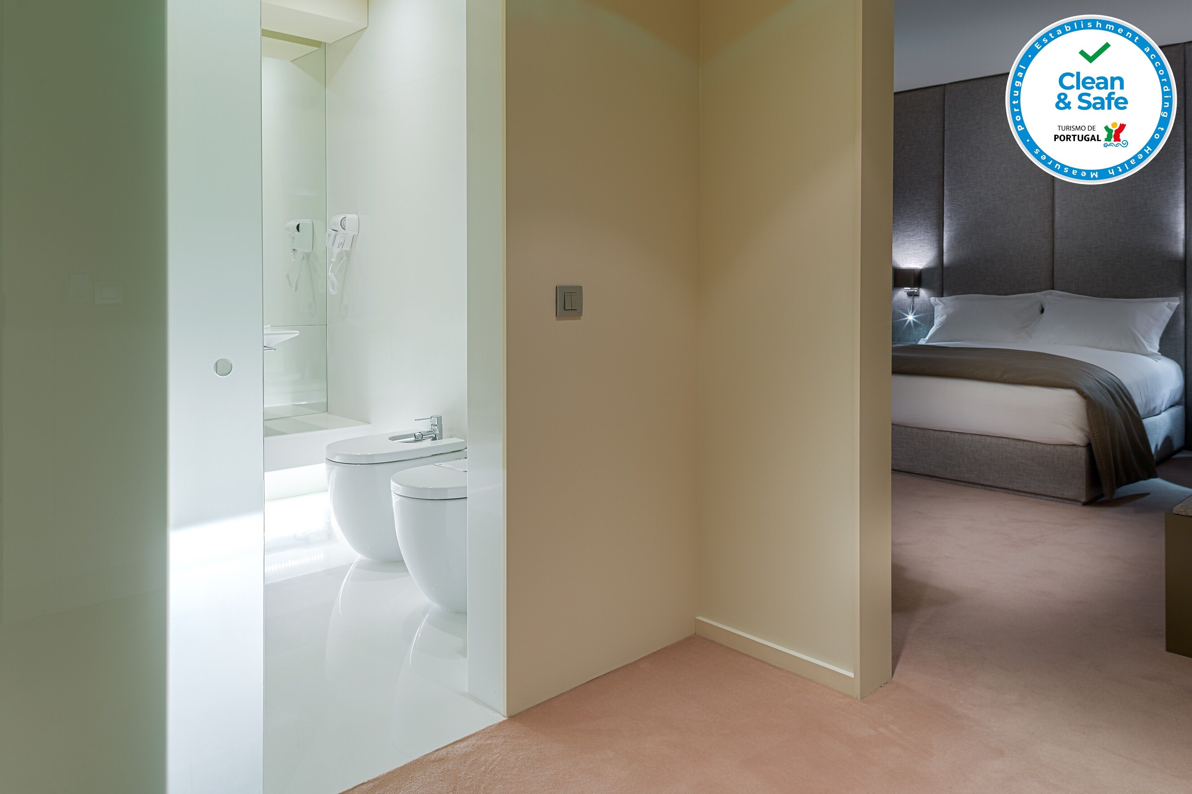 Una habitación de hotel moderna con una cama grande, baño independiente con inodoro y lavabo, y un diseño limpio y minimalista.