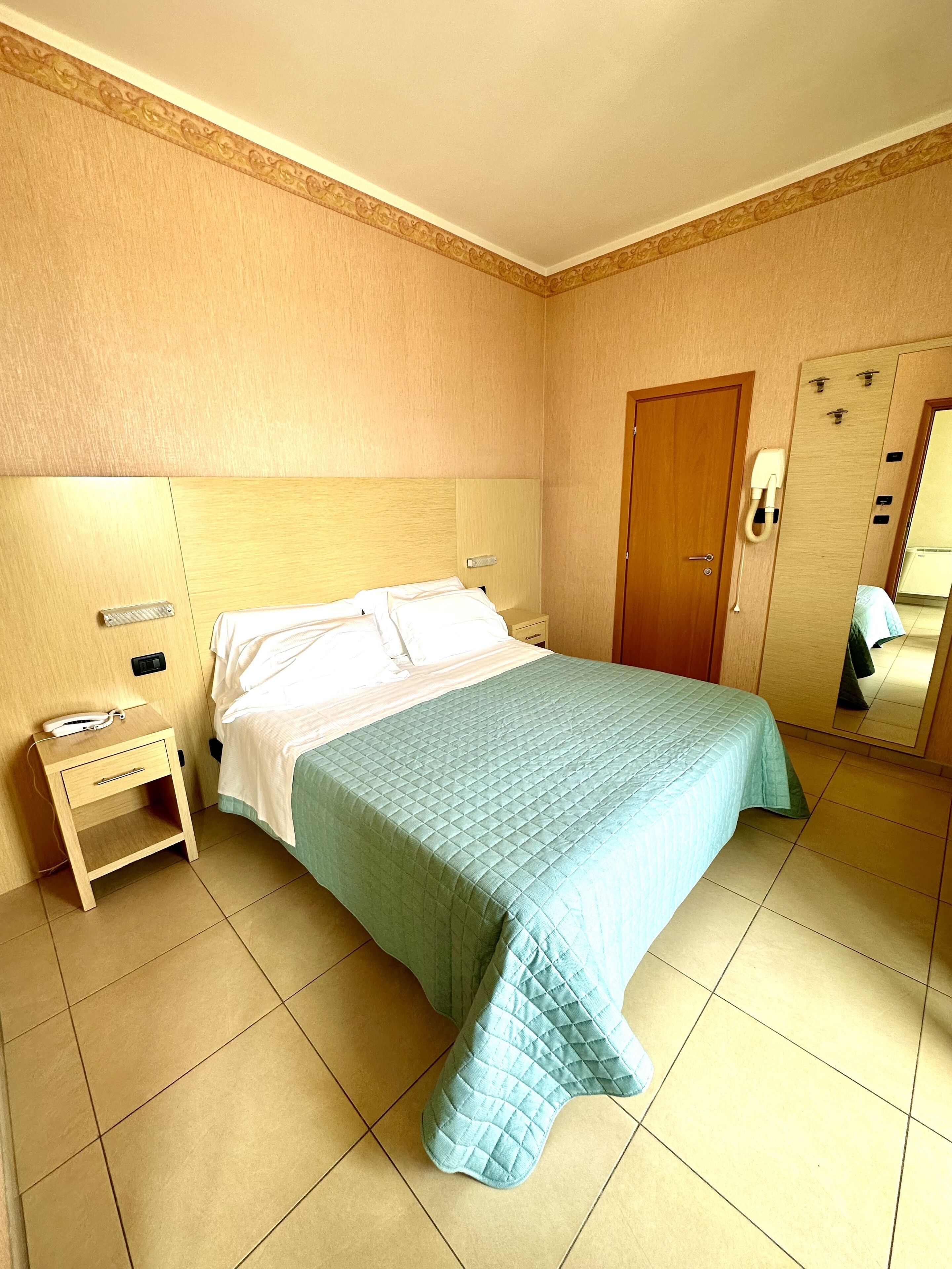 Una habitación de hotel con una cama, una mesita de noche, un teléfono y un espejo.