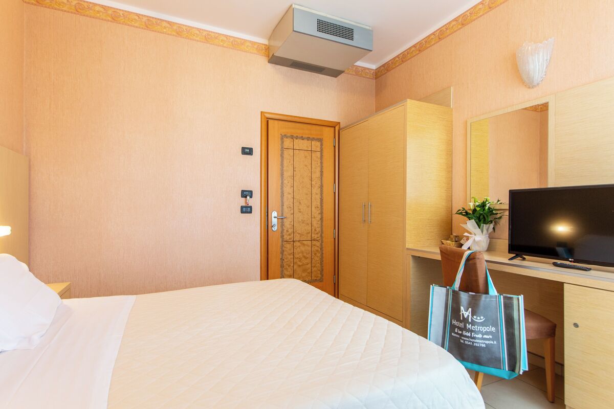 A hotel room with a bed, a desk with a television, a wardrobe, and a bathroom door.