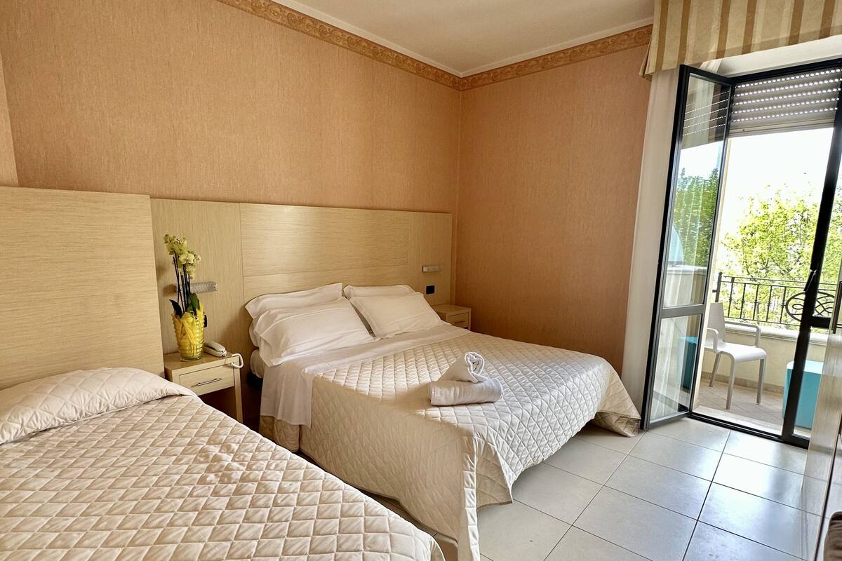 Camera d'albergo con due letti, un comodino con un telefono e vista sul balcone esterno.