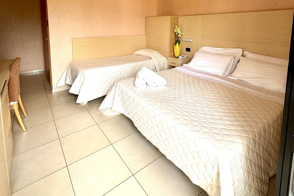 Una camera d'albergo con due letti, una scrivania e una sedia.