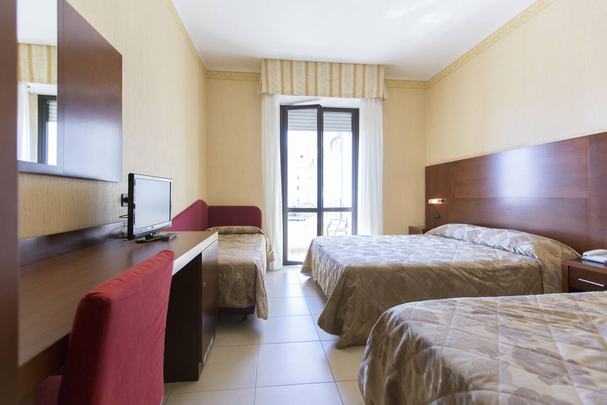 Camera d'albergo con due letti, una scrivania con un computer, una sedia e una finestra con tende.