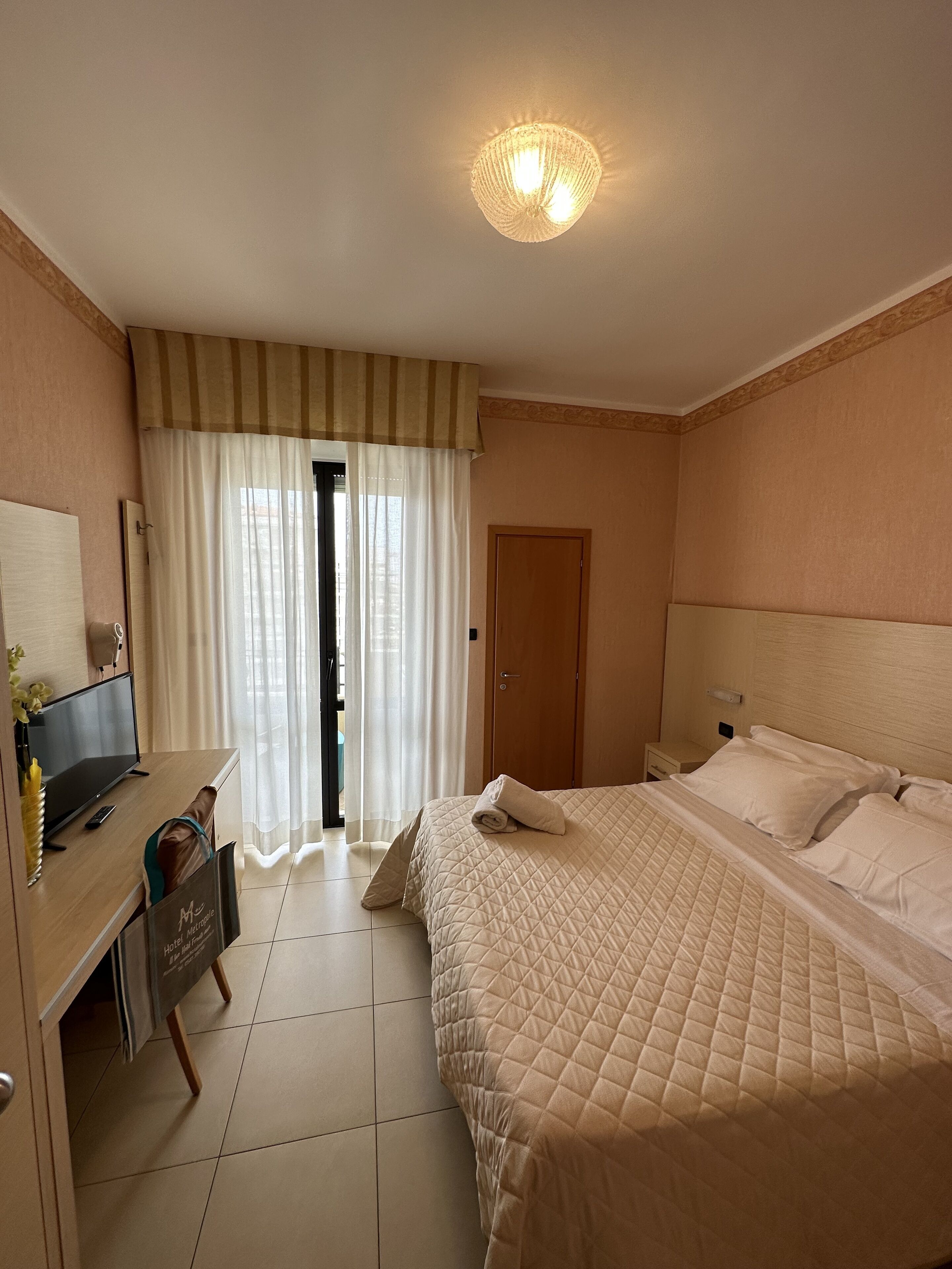 A hotel room with a bed, a desk with a computer, a television, and a bathroom door.