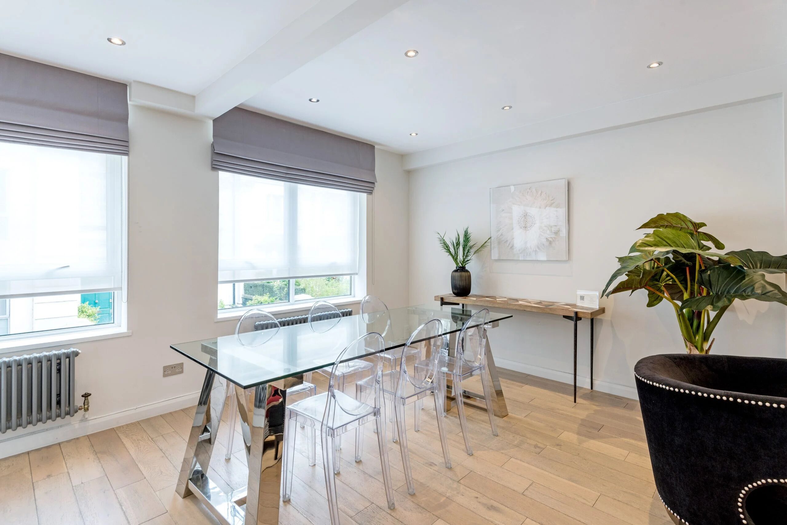 Uma área de jantar moderna com mesa de vidro e cadeiras, um vaso de planta e vista para o exterior.