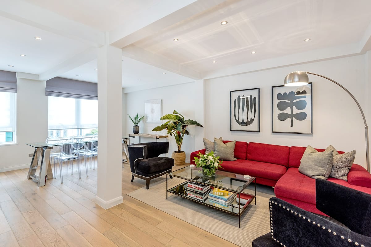 A modern living room with a red sofa, black armchairs, and a glass coffee table. There are two framed artworks on the wall and a potted plant on the floor.
