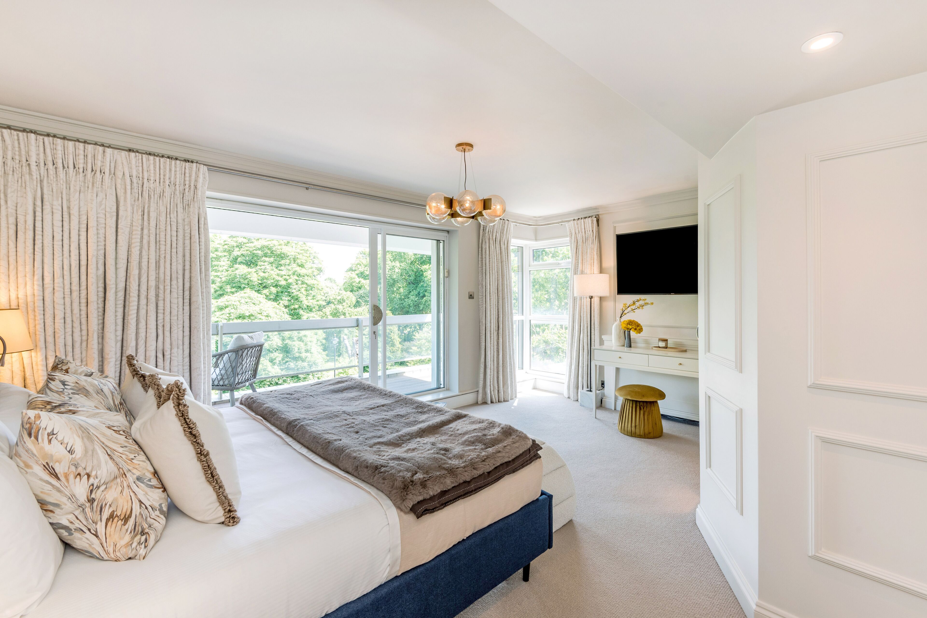 A bedroom with a large bed, a desk, and a view of greenery outside.