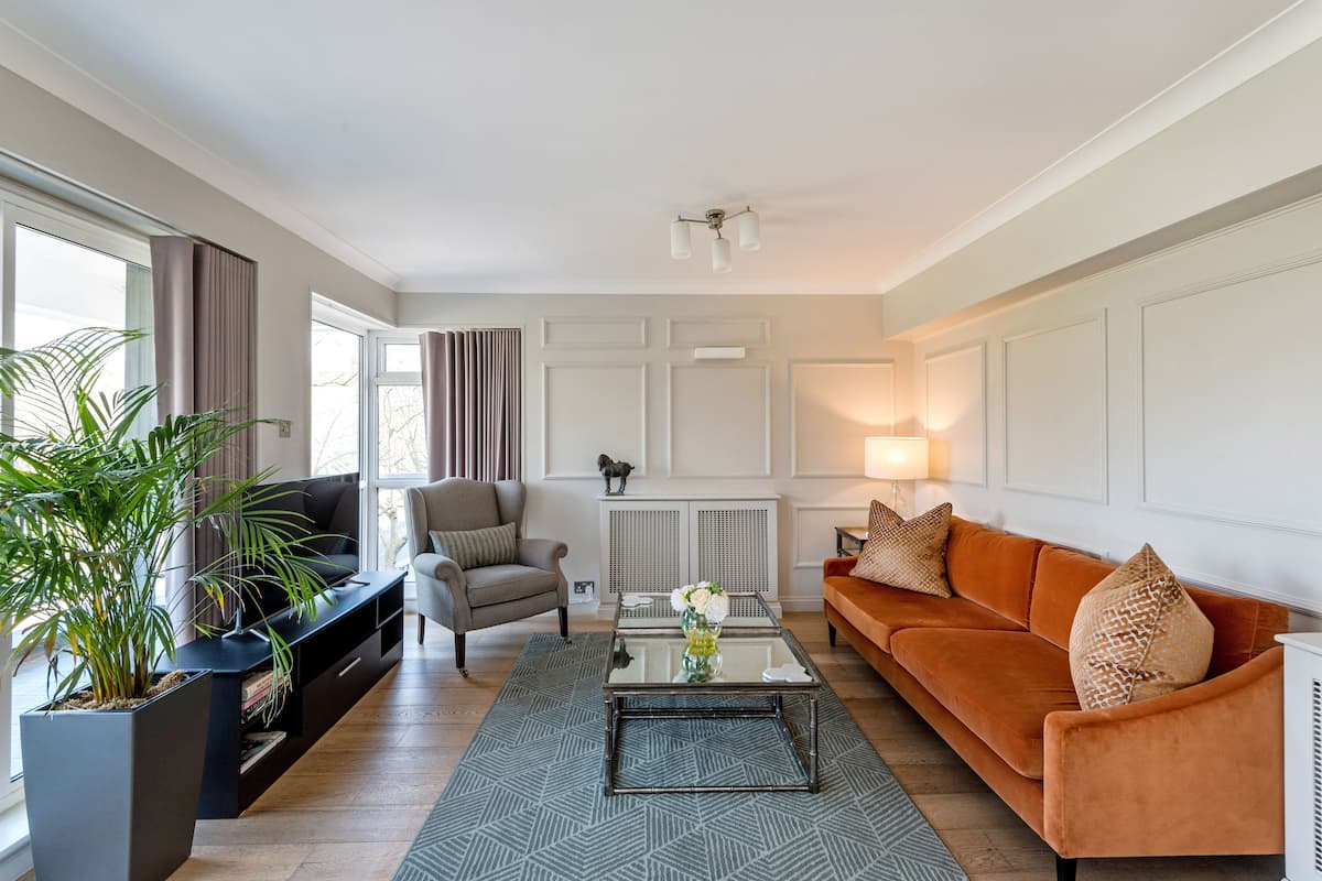 A living room with a sofa, armchair, coffee table, and a large potted plant.