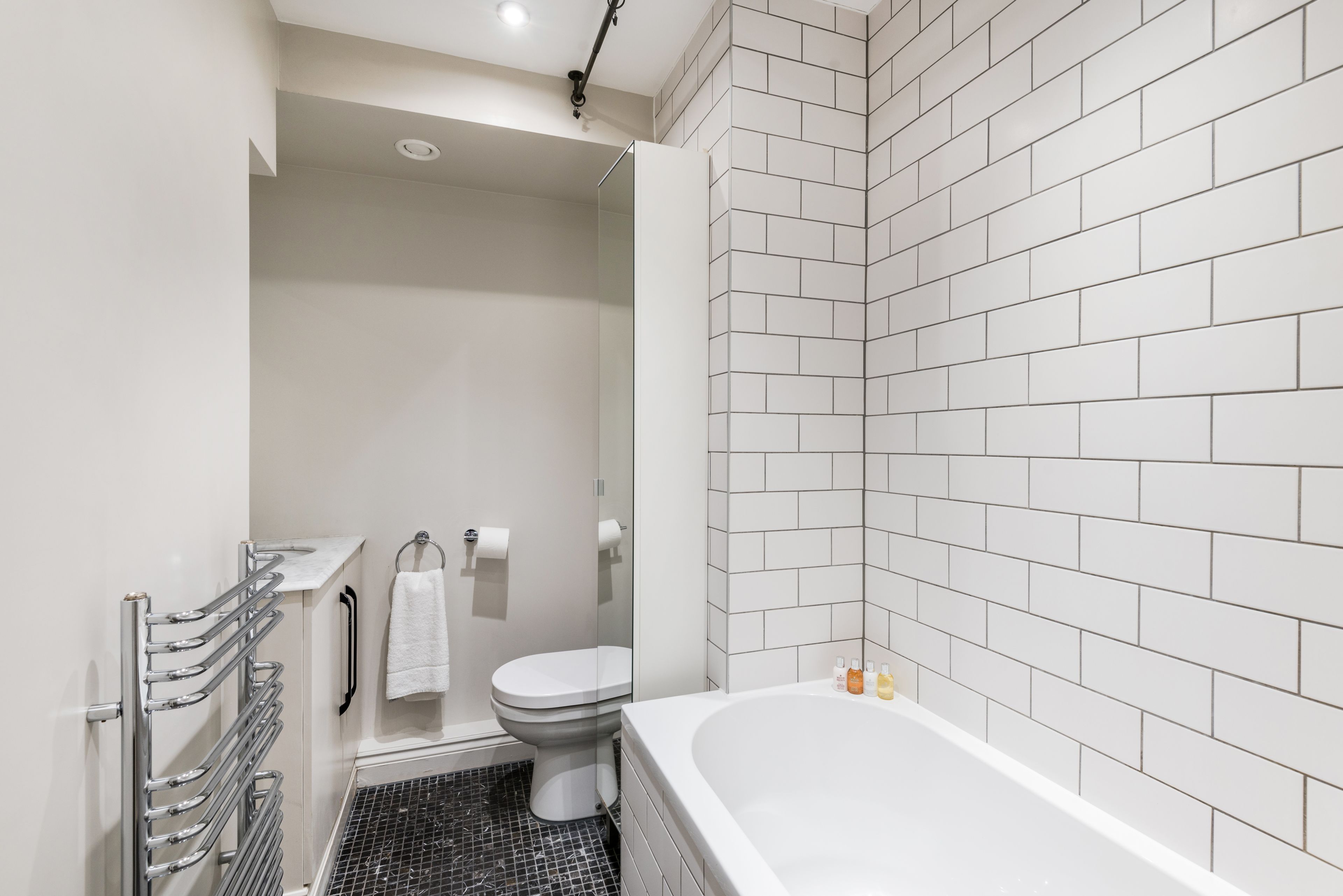 A modern bathroom with a white tiled shower, a white bathtub, and a toilet.