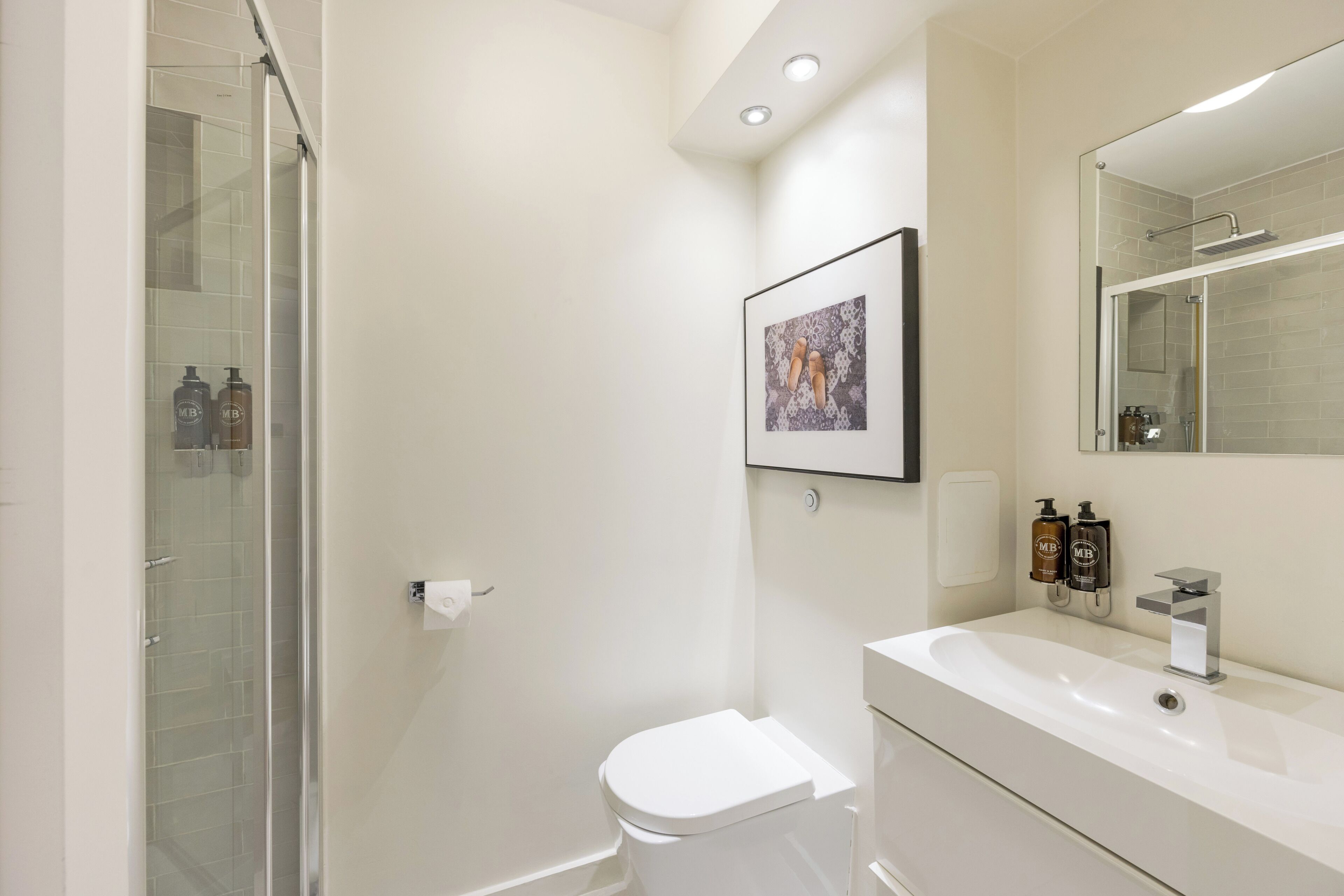 A modern bathroom with a glass shower enclosure, a white toilet, a large mirror, and a vanity with toiletries.